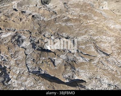 Vue aérienne rapprochée de la surface d'un glacier, révélant des textures complexes de glace, de neige et de formations rocheuses Banque D'Images