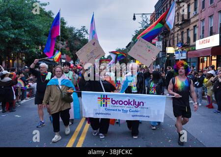 Une scène de défilé dynamique Brooklyn Pride mettant en vedette divers participants portant des drapeaux arc-en-ciel, des panneaux et une grande bannière pour le Brooklyn Community PRID Banque D'Images