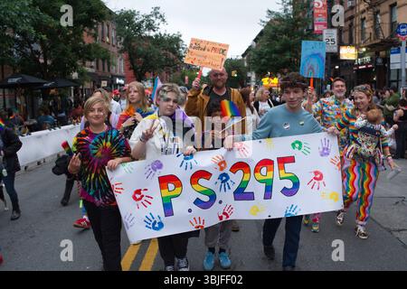 Un groupe d'enfants et d'adultes, dont beaucoup arborent des vêtements et des affiches sur le thème de l'arc-en-ciel, défilent dans une parade de rue. Ils portent une grande bannière avec 'PS.295' Banque D'Images