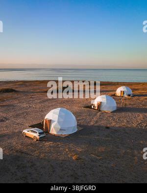 Trois dômes géodésiques modernes situés sur les rives sablonneuses du lac Issyk Kul, offrant une expérience de glamping unique sous un ciel dégagé Banque D'Images