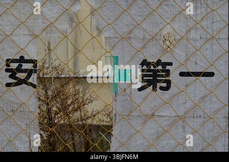 Le treillis de construction délavé derrière une clôture en fil jaune affiche le slogan de sécurité « 安全第一 » (la sécurité d’abord) en kanji noir gras Banque D'Images