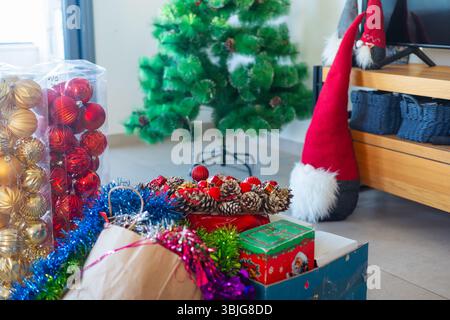Boîtes d'ornements de Noël, guirlandes et un arbre artificiel dans un salon pendant les préparations de décoration de vacances Banque D'Images