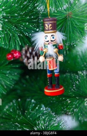 Gros plan d'un ornement festif d'arbre de Noël en forme de soldat batteur en bois avec des cheveux blancs et un tambour rouge, suspendu à une branche de pin vert luxuriant Banque D'Images