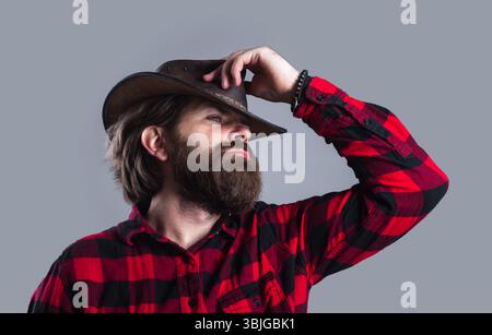 Chapeau de cow-boy. Homme barbu en chemise à carreaux et chapeau de cow-boy. Cow-boys en chapeau en cuir et chemise à carreaux. Portrait d'un jeune beau macho barbu en cow-boy Banque D'Images