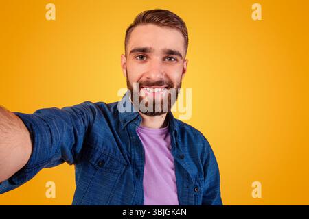 Beau jeune homme caucasien prenant le selfie et souriant largement arrière-plan orange studio Banque D'Images
