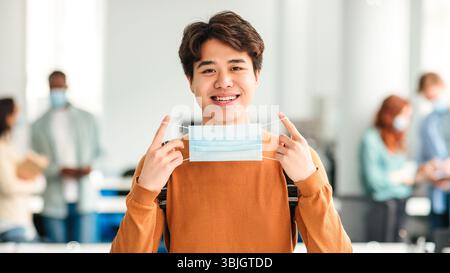 Homme asiatique montrant un masque médical à l'université Banque D'Images