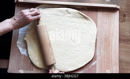 Vue de dessus des mains de la femme roulant la pâte sur la table en bois avec rouleau à pâtisserie en bois. Cuisson maison, cours de cuisine étape par étape, préparation, pâtisserie Banque D'Images