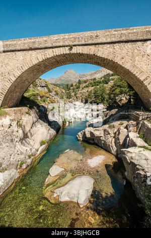 Le pont Ponte Altu à Albertacce sur l'île méditerranéenne de Corse passant au-dessus du fleuve Golo limpide avec Monte Albanu au loin Banque D'Images