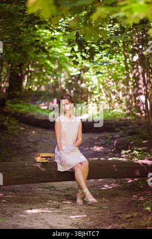 moscou, russie,07.07.2022 Une jeune femme caucasienne aux cheveux bruns est assise sur une bûche dans une forêt verdoyante. La lumière du soleil filtre à travers les feuilles, créant Banque D'Images