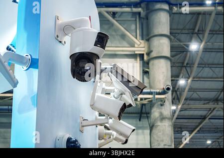 Système de surveillance moderne avec différentes caméras de sécurité (PTZ, Bullet) montées sur une structure dans un bâtiment industriel/commercial. Met l'accent sur la technol Banque D'Images