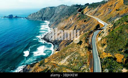 Route côtière sinueuse le long de falaises accidentées. Une vue aérienne spectaculaire d'une route côtière sinueuse enserrant des falaises abruptes à côté d'un océan turquoise. Banque D'Images