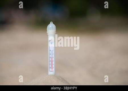 Un thermomètre montrant 33 degrés Celsius coincé dans le sable sur une plage de sable. Copier l'espace. Arrière-plan. Banque D'Images