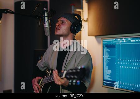 Homme passionnément chantant et jouant de la guitare dans un studio d'enregistrement professionnel Banque D'Images