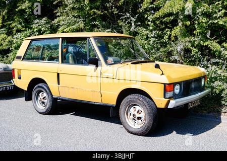 Vintage années 1970 jaune Range rover SUV garé sur une rue ensoleillée avec feuillage vert dans le style rétro classique en arrière-plan Banque D'Images