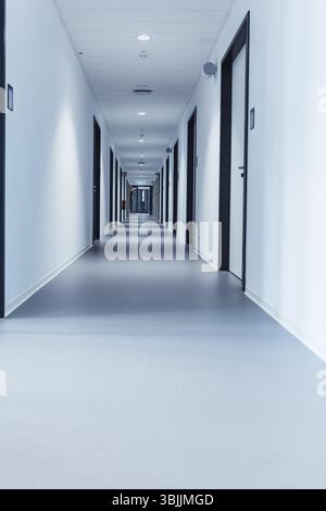 Un long couloir étroit d'une école moderne ou d'un immeuble de bureaux avec plusieurs portes fermées Banque D'Images