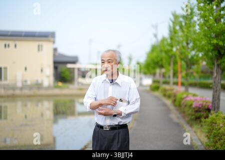 Dans les campagnes japonaises, un Japonais de la fin des années 70 marche le long d'une route agricole entourée de larges rizières. Il porte une chemise blanche et un chapeau, appréciant le fr Banque D'Images