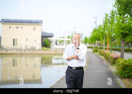 Dans les campagnes japonaises, un Japonais de la fin des années 70 marche le long d'une route agricole entourée de larges rizières. Il porte une chemise blanche et un chapeau, appréciant le fr Banque D'Images
