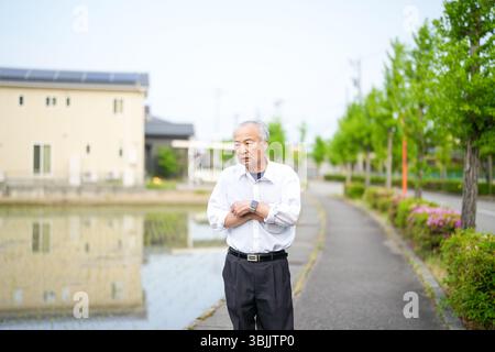 Dans les campagnes japonaises, un Japonais de la fin des années 70 marche le long d'une route agricole entourée de larges rizières. Il porte une chemise blanche et un chapeau, appréciant le fr Banque D'Images