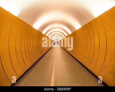 Stockholm, Suède - 11 mai 2025 : un long tunnel incurvé avec des murs jaunes lisses et un plafond lumineux et éclairé. La perspective crée un sens Banque D'Images