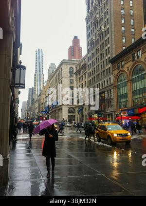 NEW YORK, États-Unis – 19 MARS 2013 : des personnes munies de parapluies marchent le long de la Cinquième Avenue sous la pluie. Des taxis jaunes et des devantures de magasins peuvent être vus. Banque D'Images