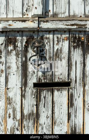 Une porte faite de planches de bois altérées présente de la peinture bleue pelable et une poignée décorative en métal Banque D'Images