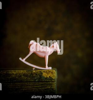 Un petit jouet de cheval à bascule rose est assis sur une étagère en bois altéré, doucement éclairé par faible luminosité. Banque D'Images