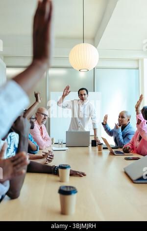 Un groupe de professionnels divers dans une salle de conférence moderne est engagé dans une réunion d'affaires. Les membres de l'équipe lèvent la main pour voter, illustrat Banque D'Images