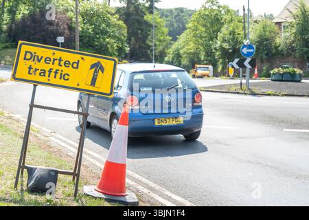 Panneau jaune de déviation le long d'un cône de circulation sur un mini rond-point avec circulation de véhicules Banque D'Images