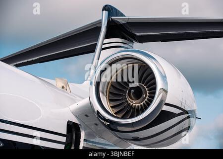 Gros plan d'un moteur à réaction sur un avion d'affaires de luxe avec queue en T, photographié sous un ciel lumineux. Pales de turboréacteur et nacelle polie dans les détails nets. Banque D'Images