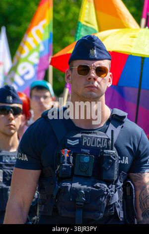 Un policier polonais en gilet tactique et lunettes de soleil se tient parmi les participants à la parade de la fierté de Varsovie à Varsovie, dans la Voïvodie de Masovie, Pologne. Juin Banque D'Images