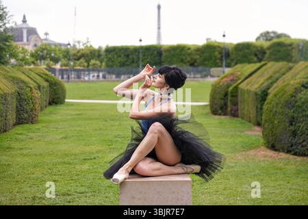 Danseuse de ballet dans une pose assise gracieuse sur un piédestal dans un parc verdoyant Banque D'Images