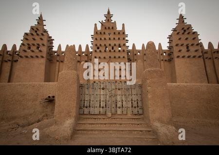 La façade de la Grande Mosquée de Djenné au Mali à l'aube, montrant sa façade emblématique en briques de boue, sa porte centrale et ses trois imposants minarets. Banque D'Images