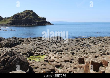 Roches de basalte hexagonales avec une grande formation rocheuse derrière une baie de la chaussée des géants dans le comté d'Antrim, Irlande du Nord Banque D'Images