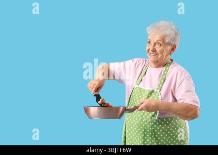 Femme senior avec des légumes dans une poêle à frire sur fond bleu Banque D'Images