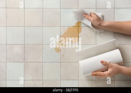 Femme essuyant le café renversé avec des serviettes en papier sur fond de tuiles blanches Banque D'Images