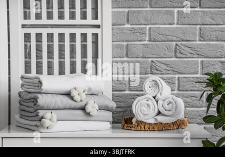 Pile de draps propres avec des fleurs de coton et des serviettes sur la table près du mur de briques grises dans la chambre Banque D'Images