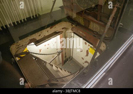 Vue d'une échelle métallique escarpée menant vers le bas d'une trappe de sous-marin usée. La peinture écaillée, le panneau d'avertissement et les tuyaux exposés donnent une impression industrielle. Banque D'Images