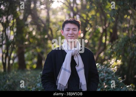 Portrait à la taille haute d'un jeune homme portant une écharpe sur un fond de forêt floue Banque D'Images