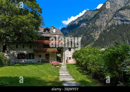 Un chemin de pierre sur une pelouse verte mène à une maison alpine traditionnelle en pierre dans la petite ville de Gressoney-Saint-Jean, Vallée d'Aoste, Italie. Banque D'Images