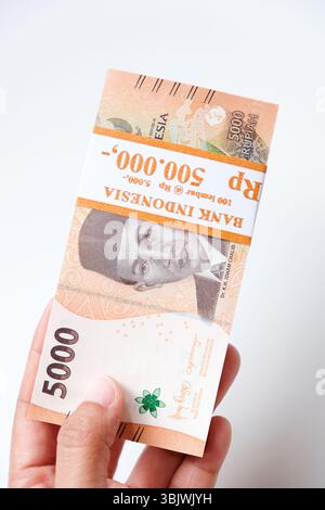 Pekanbaru, Indonésie - 21 mars 2025 : main tenant des billets de banque rupiah indonésiens RP 5,000 isolés sur fond blanc pour THR sur Eid al-Fitr ou Lebara Banque D'Images