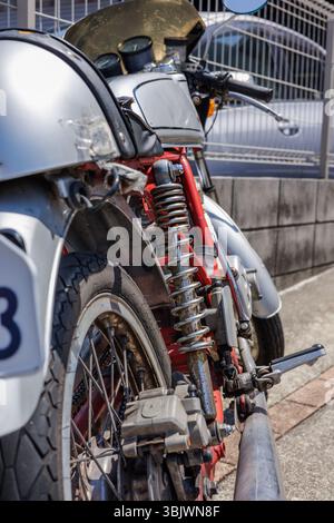 Vue arrière rapprochée de la moto vintage met en évidence ses pièces mécaniques détaillées - système de suspension et roue. Vélo est garé sur le côté ensoleillé de la rue. Banque D'Images