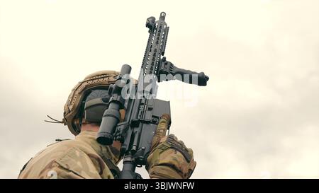 Soldat tenant un fusil dans un équipement tactique. Gros plan d'un soldat tenant un fusil, vêtu d'un équipement tactique complet, y compris un casque et des gants. Banque D'Images