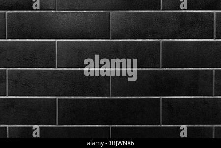 Fond de mur de carreaux rectangulaires noirs. Gros plan d'un mur avec des carreaux rectangulaires noirs disposés en motif horizontal. Banque D'Images