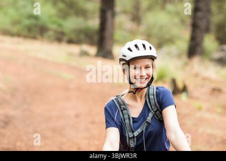 Femme à vélo portant un casque blanc et un pack d'hydratation gris sur le sentier rouge de forêt de terre Banque D'Images