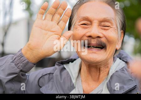 Portrait de tête photographié homme mûr heureux agitant la main, disant bonjour, regardant la caméra à l'extérieur. Homme plus âgé amical faisant un appel vidéo à des parents ou ven Banque D'Images