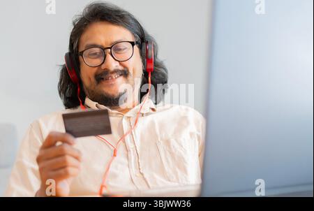 Photo d'un bel homme asiatique mature assis sur son canapé à la maison et utilisant son ordinateur portable pour des achats en ligne. Mise au point sélective. Banque D'Images