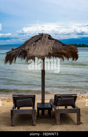 Parasol est installé sur le sable à côté de deux chaises de plage. Le parapluie est ouvert et les chaises sont vides. La scène est paisible et relaxant, avec Banque D'Images