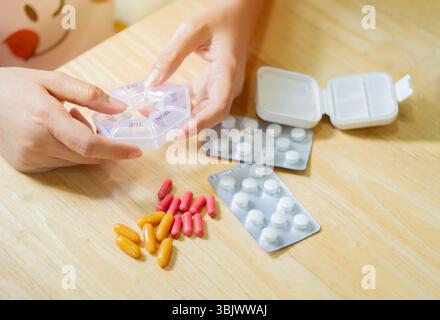 Gros plan des mains féminines mettant des pilules dans des récipients en plastique, des mains avec des pilules et des pilules. Concept de routine de pharmacie. Banque D'Images