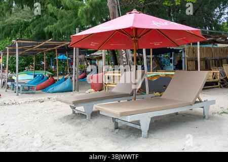 Gili, Lombok, Indonésie - 3 janvier 2025 : plage avec un parasol rouge et deux chaises longues bronzées. Les chaises sont vides Banque D'Images