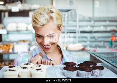 Femme dans la vingtaine penchée sur le comptoir d'affichage de boulangerie examinant des muffins givrés et au chocolat Banque D'Images